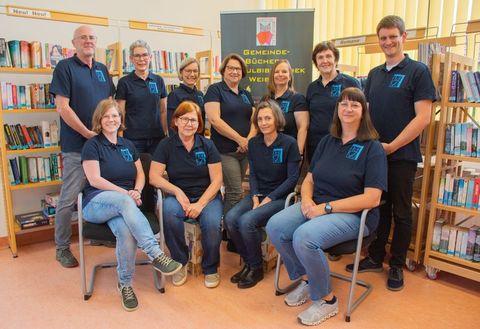 Büchereiteam sitzend und stehend vor Bücherregalen